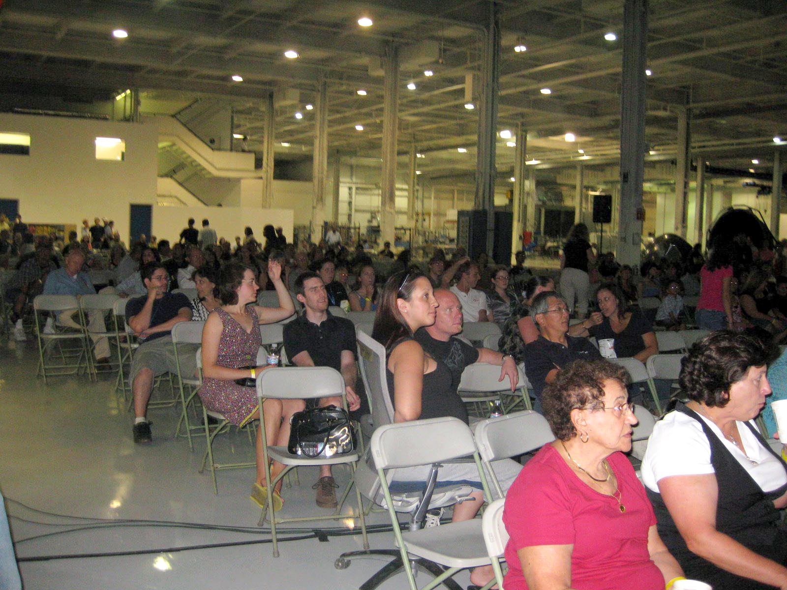 SpaceX employees and their families sit on folding chairs in the Hawthorne hangar, waiting for the Flight 3 launch.