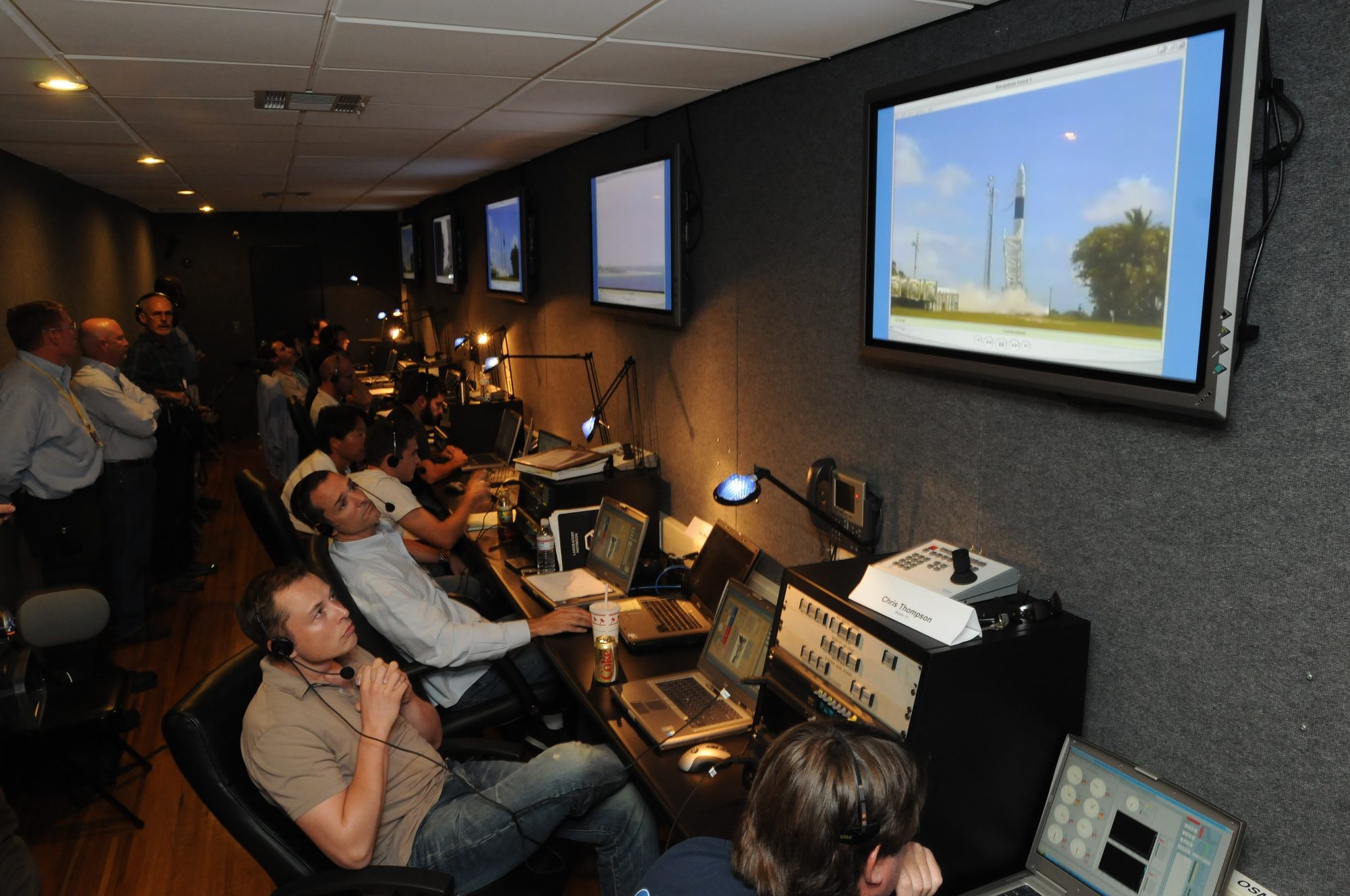 Elon Musk, in headphones, and the team in the Hawthorne control trailer look up at the Flight 4 launch on a wall screen.