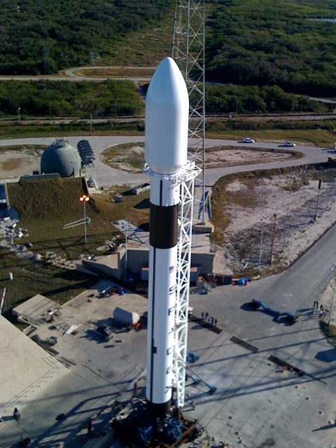 Falcon 9 seen from high on the lightning tower beside it, the pad and the Cape below.
