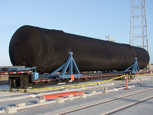 The Falcon 9 first stage tank on its truck at Cape Canaveral in daylight.