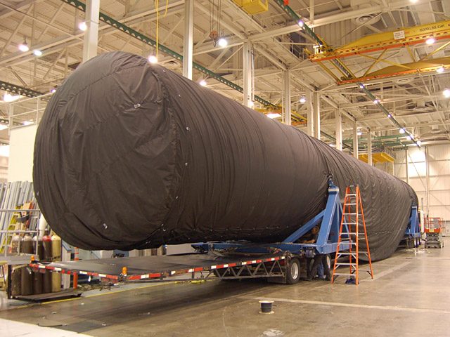 The Falcon 9 first stage tank on its shipping cradles, wrapped in a fitted tarp.