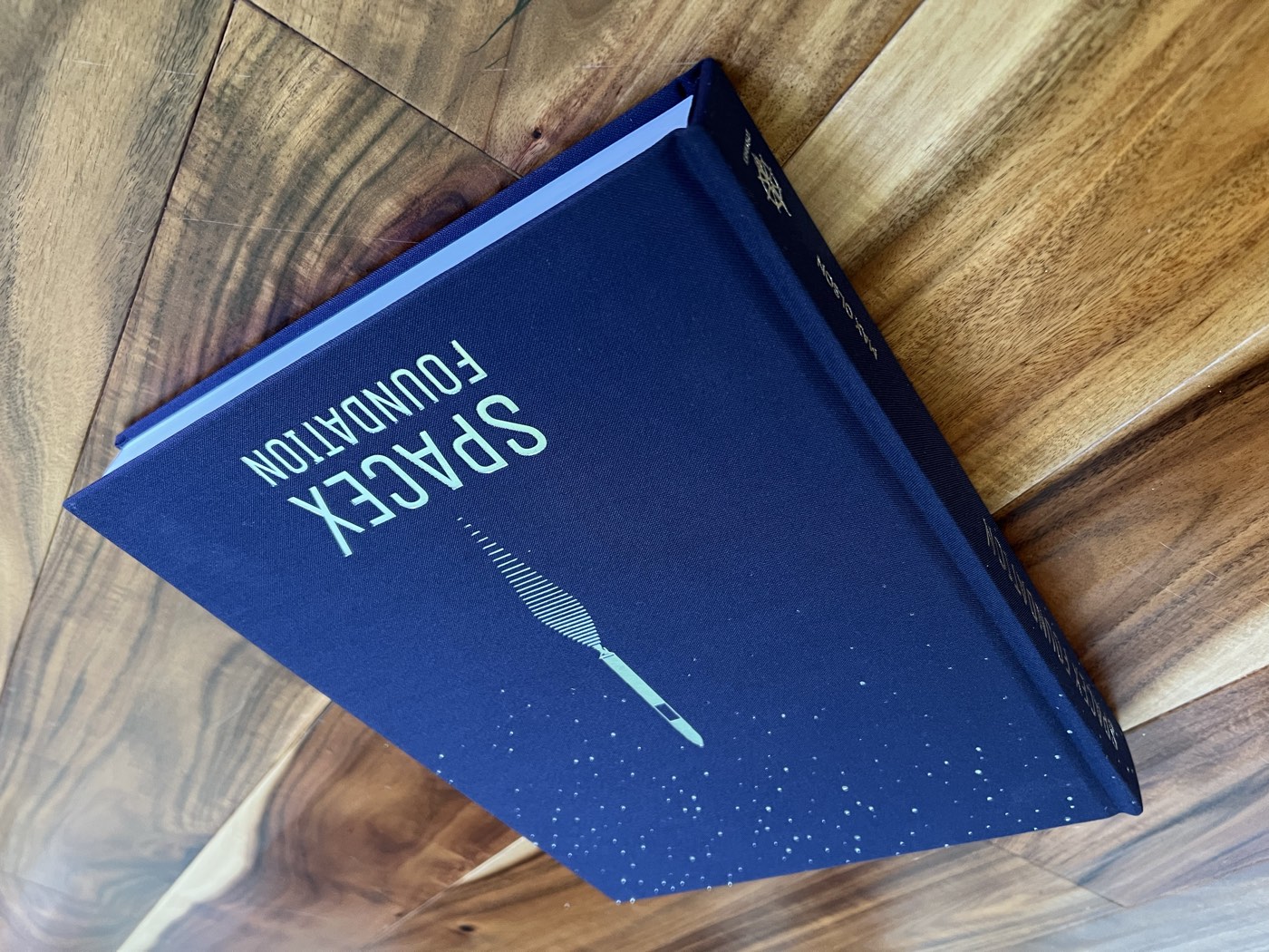 SpaceX Foundation, a navy cloth hardcover with a foil star field and title, on a wooden table
