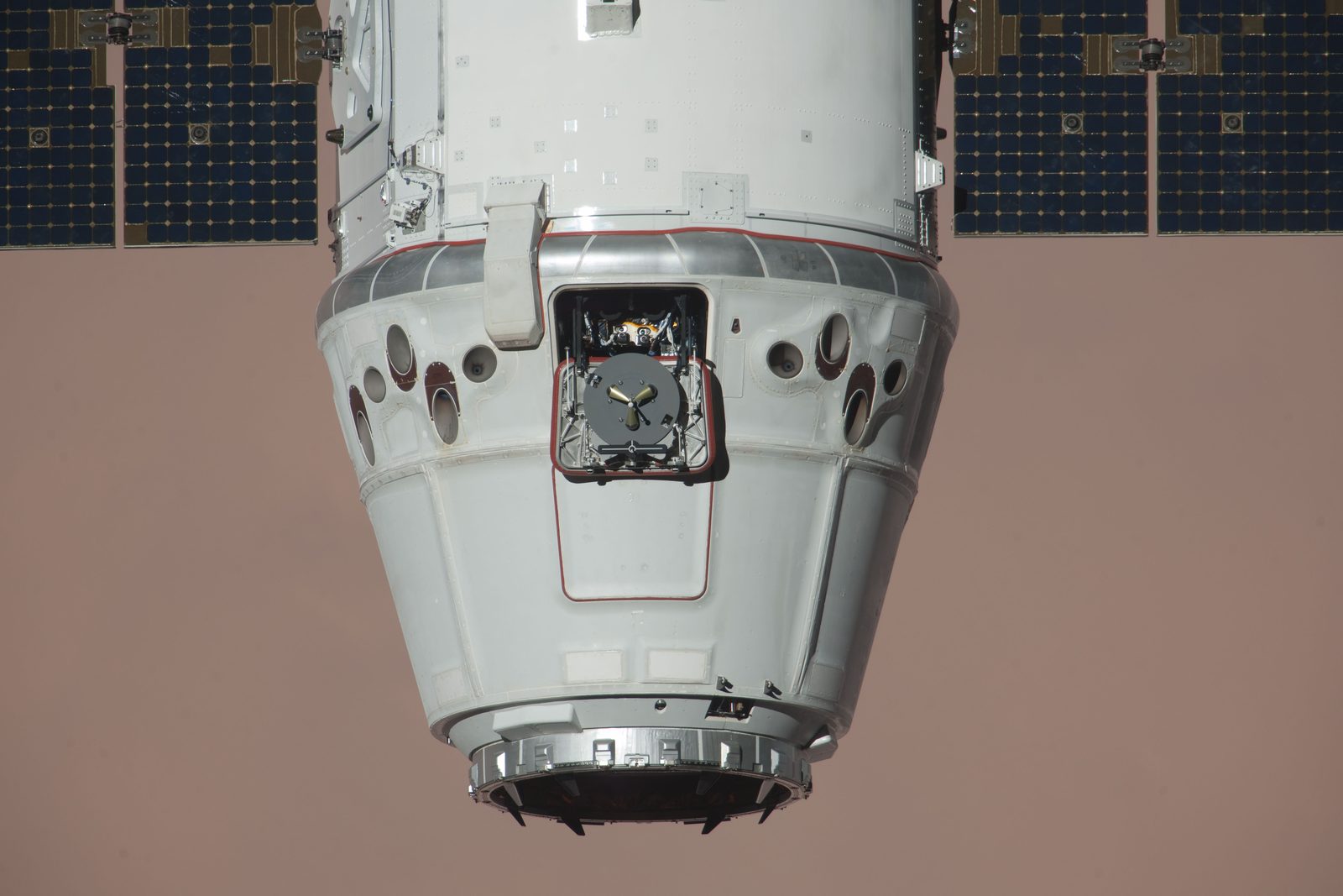 Close view of Dragon from below, its capsule and trunk filling the frame, over reddish desert.