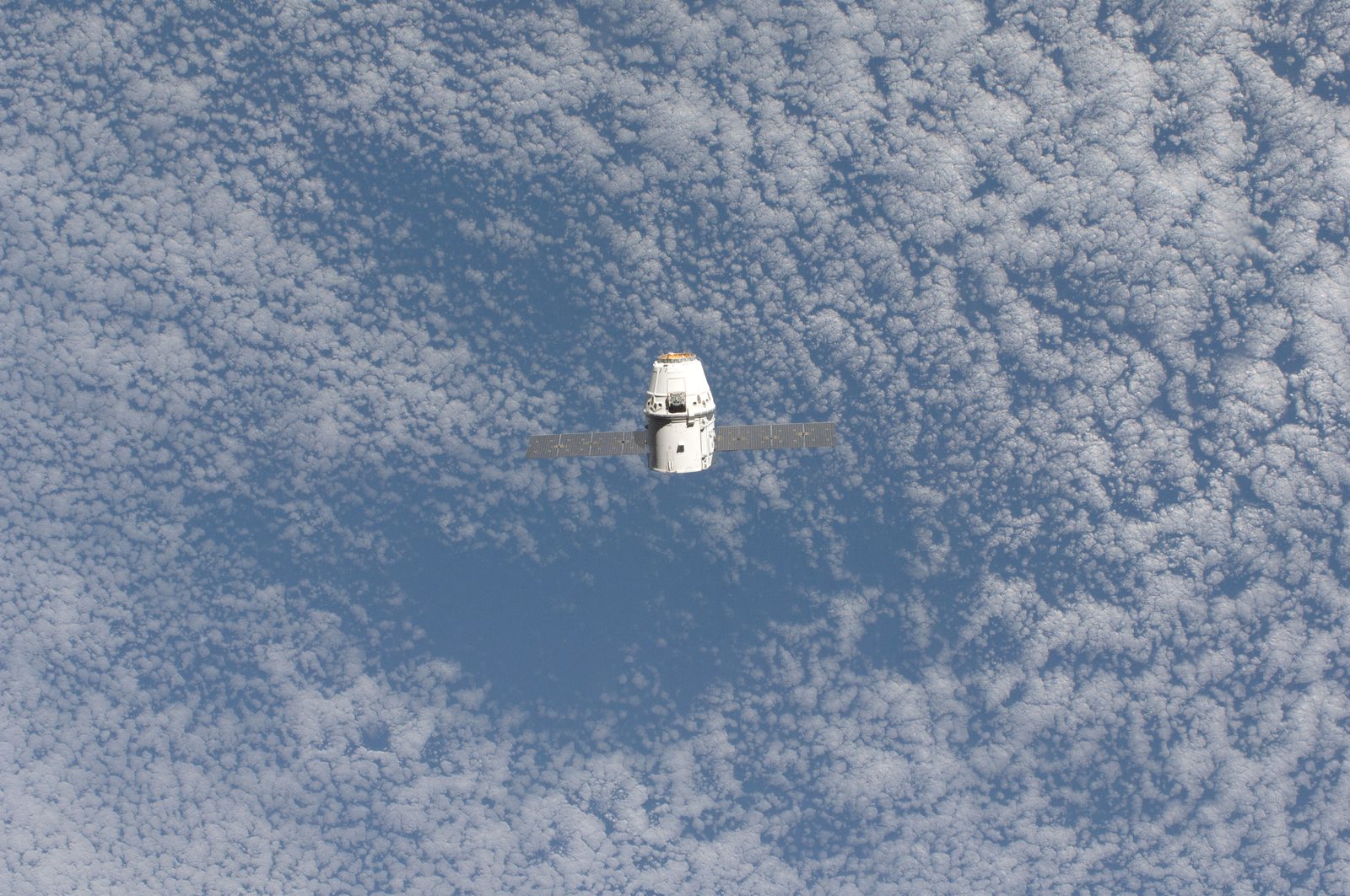 Dragon, small at center, over a field of broken cloud.