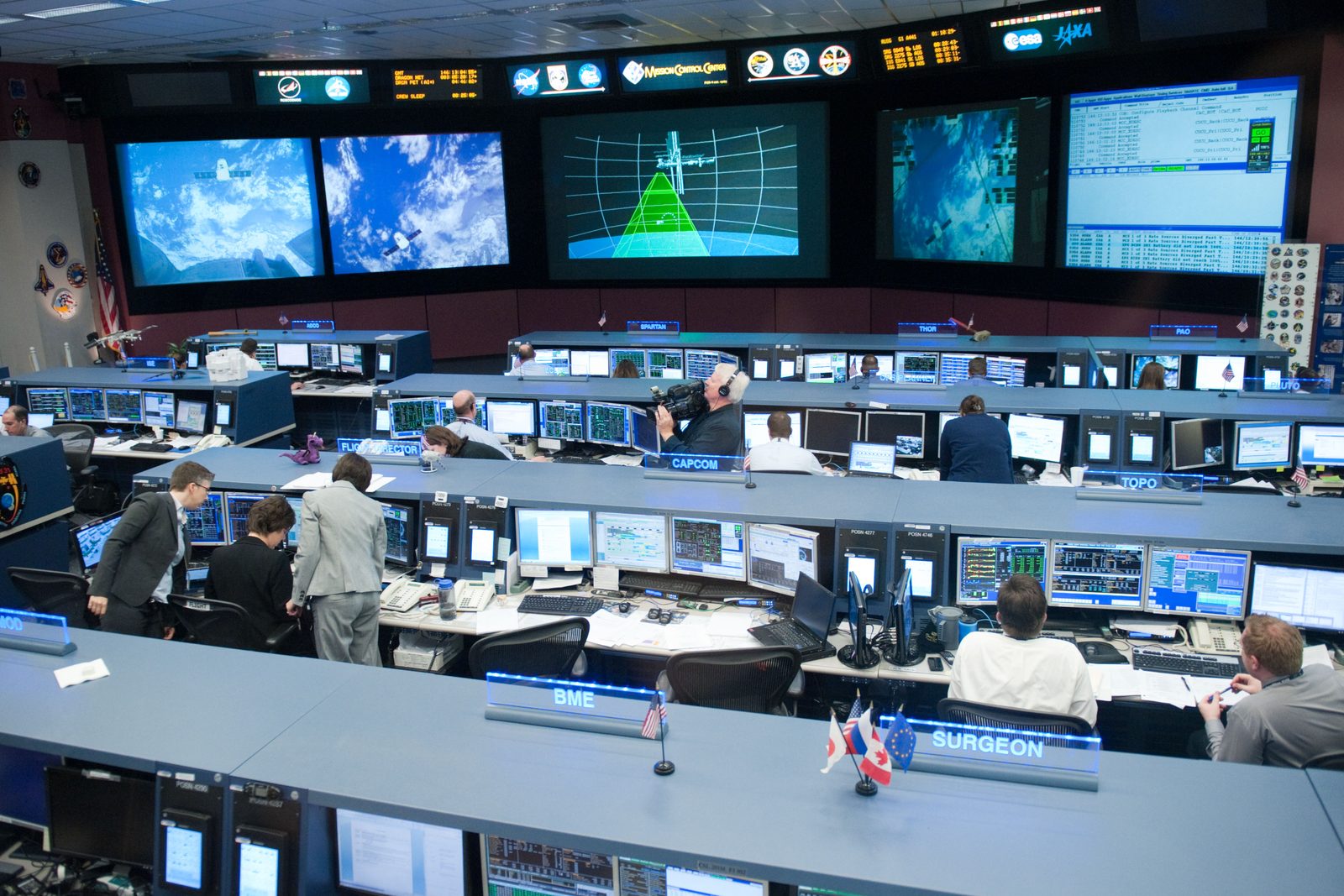 Houston's flight control room: rows of consoles, with views of Dragon and the approach on the front screens.