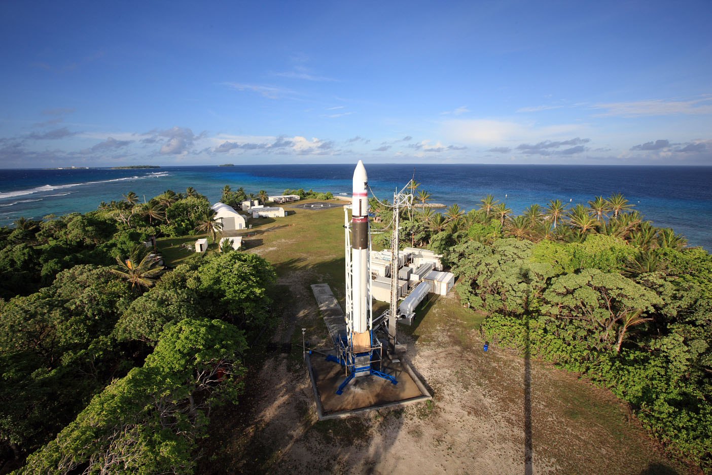 Falcon 1 stands on its pad on Omelek, a small green island ringed by reef, with the Pacific behind it.
